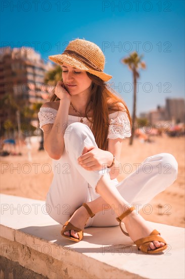 A Caucasian redhead dressed in white and with a straw hat on the beaches of Calpe