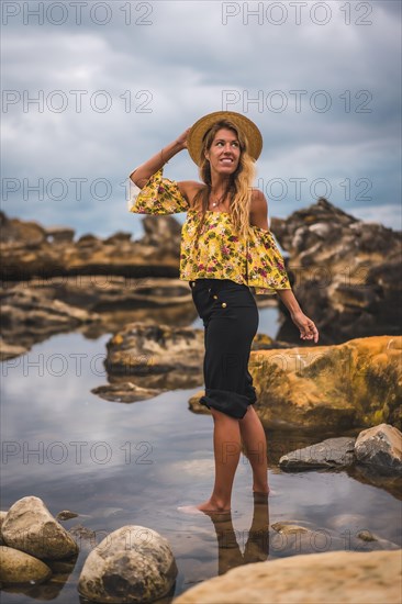 Girl in a floral shirt and black shorts in a natural landscape by the sea at sunset