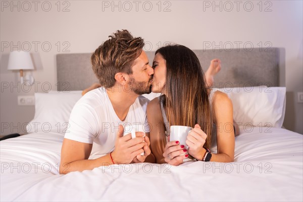 Kiss of a loving couple in pajamas having breakfast in the hotel bed