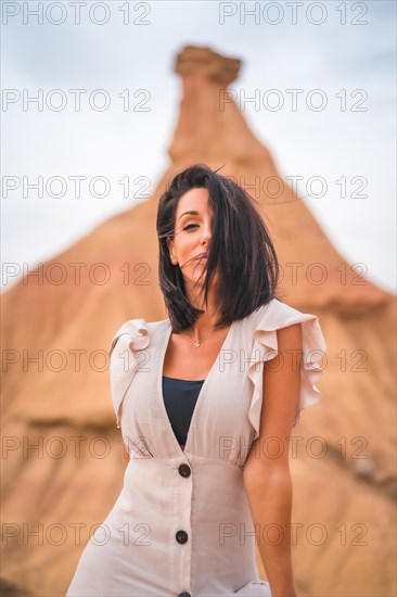 Sensual gazes from a brunette Caucasian girl in an explorer outfit with a white dress in a desert on a cloudy afternoon