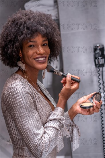 A young black girl with afro hair putting on makeup before the party with a smile. Exclusive party