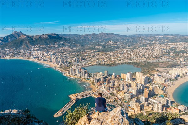 A young man sitting on top of the Penon de Ifach Natural Park in Calpe