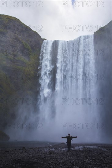 A tourist with open arms at the bottom of the Skogafoss waterfall in the golden circle of the south of Iceland