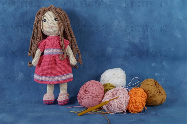 Amigurumi doll handmade on a blue background with the yarns used for its elaboration