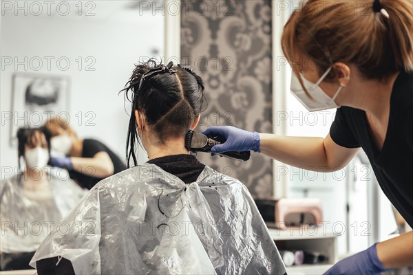 Hairdresser with mask shaving with razor. Reopening with security measures of Hairdressers in the Covid-19 pandemic