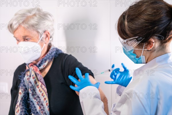 An elderly woman receiving the injection of the coronavirus vaccine by a doctor to receive the antibodies