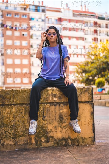 Dark-skinned young man in a purple T-shirt with long braids and purple glasses sitting on a yellow cement loft