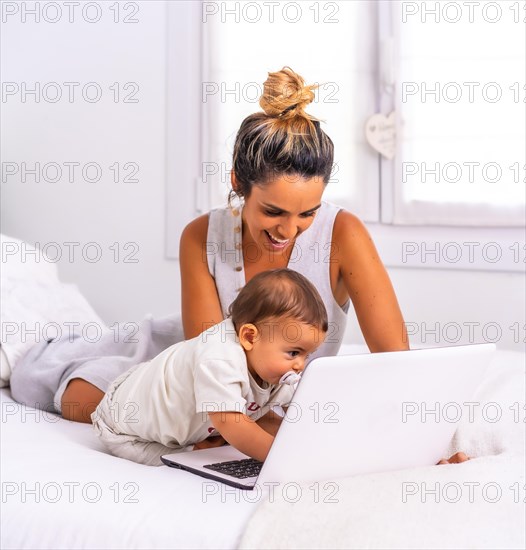 Young Caucasian mother with her son in the room on top of the bed. Drink less than a year in a video call with her family. Communication with grandparents in the confinement of the covid-19 pandemic