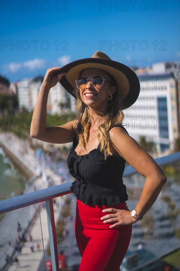 Blonde woman spending the holidays in a luxury hotel on a terrace wearing a hat with sunglasses