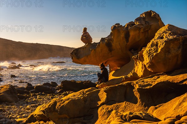 A relaxed young woman looking at the sea at sunset in the cove of stones on the Jaizkibel mountain in the town of Pasajes near San Sebastian. Basque Country