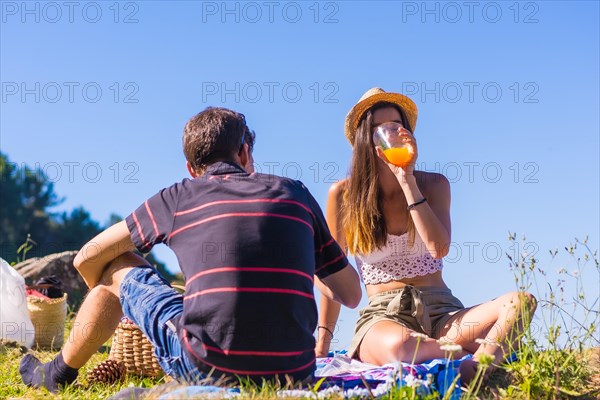 A young Caucasian couple at the picnic drinking orange juice in the mountains by the sea enjoying the heat