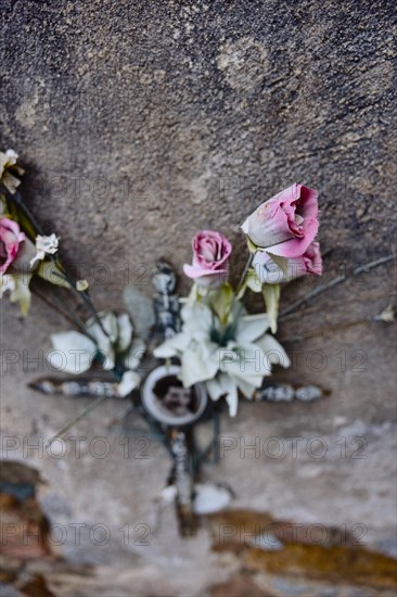 Artificial roses behind a cross on a weathered wall on a grave in a cemetery