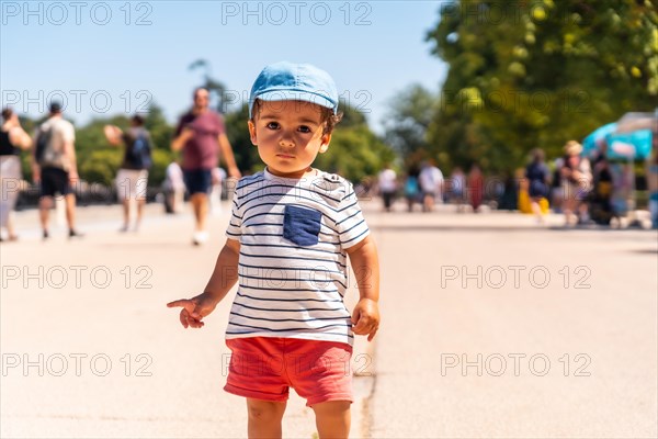 Portrait of a one year old Caucasian boy looking at the camera walking in a park with a cap