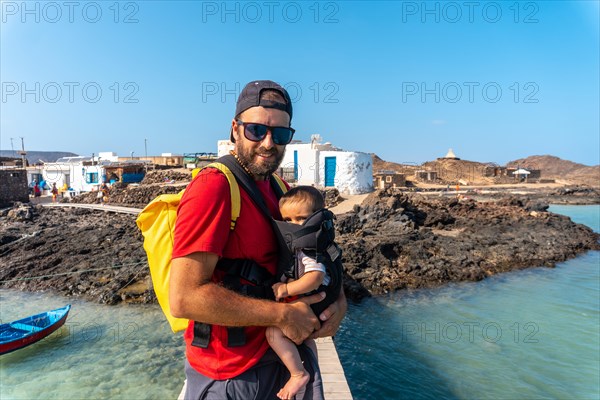 A young father with his son on the wooden walkway by the sea on Isla de Lobos