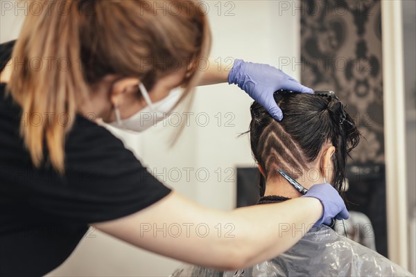 Hairdresser with mask shaving and drawing the client. Reopening with security measures of Hairdressers in the Covid-19 pandemic