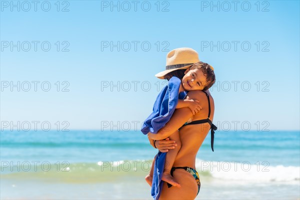 Mother with hat hugging and having fun with her son by the sea