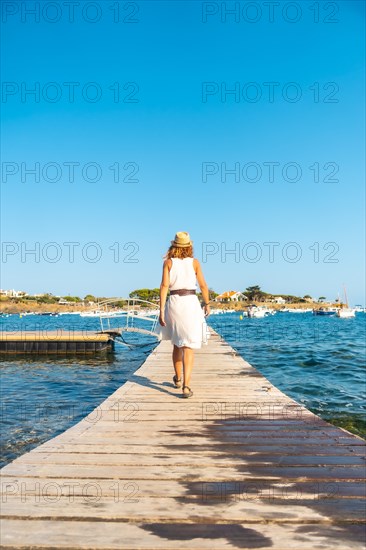 A young woman in a dress in Cadaques walking along a wooden footbridge by the sea