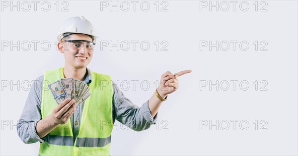 Smiling young engineer holding money pointing aside isolated. Handsome male engineer showing money pointing an advertisement isolated
