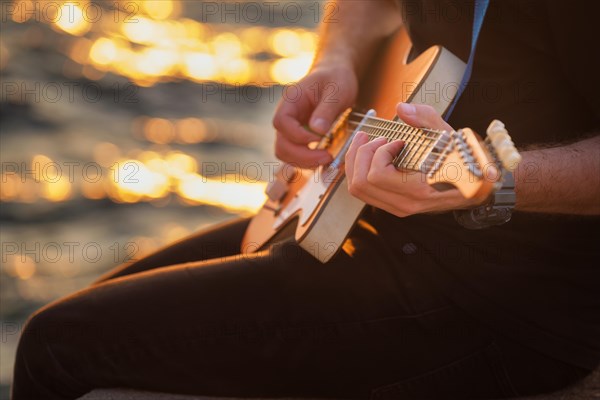 Street musician playing electric guitar hands with guitar pick close up with water in background