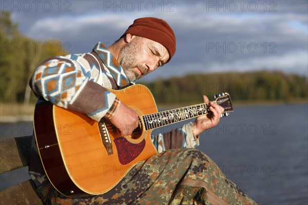 Man playing guitar on a jetty by the lake