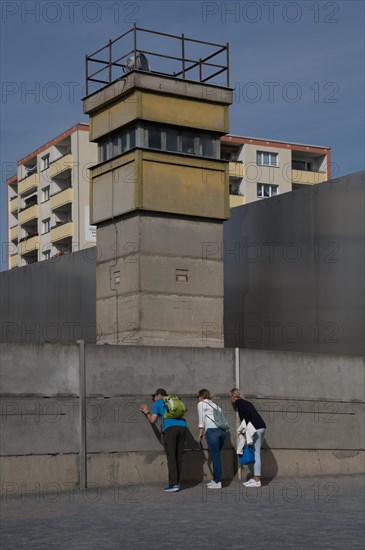 Visitors to the Wall memorial look through gaps between the concrete slabs at a section of the former death strip