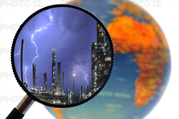 Lightning during thunderstorm above petrochemical industry seen through magnifying glass held against illuminated terrestrial globe