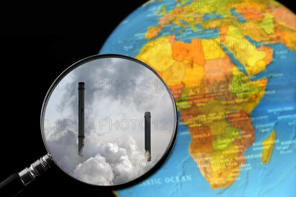 Chimneys covered in smoke seen through magnifying glass held against illuminated terrestrial globe