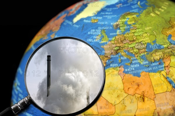 Chimneys covered in smoke seen through magnifying glass held against illuminated terrestrial globe