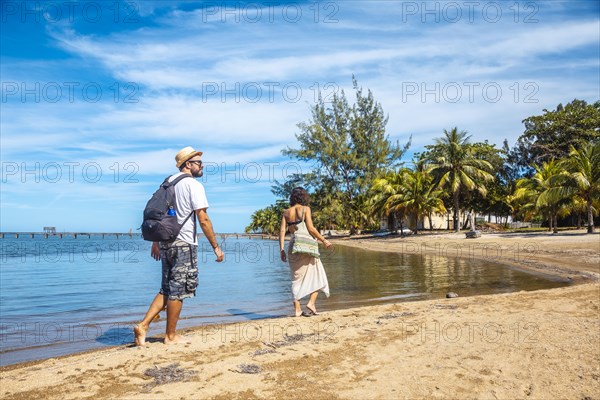 Two young people walking along the beach of Sandy Bay on Roatan Island. Honduras