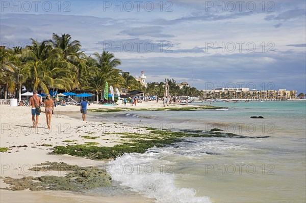 Western tourists walking on white sandy beach and hotels along Playa Del Carmen