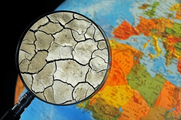 Cracked earth by drought seen through magnifying glass held against illuminated terrestrial globe