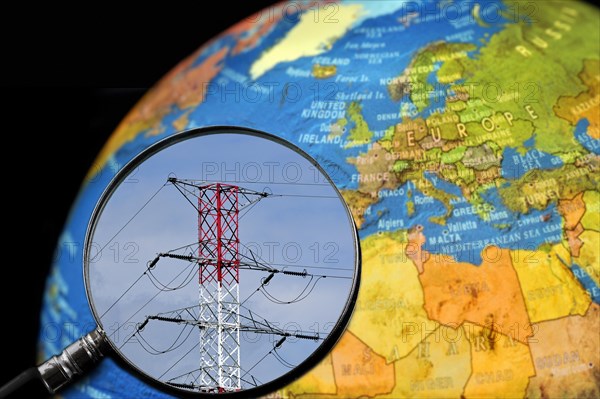 High voltage pylon in red and white through magnifying glass held against illuminated terrestrial globe