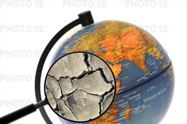 Cracked earth by drought seen through magnifying glass held against illuminated terrestrial globe