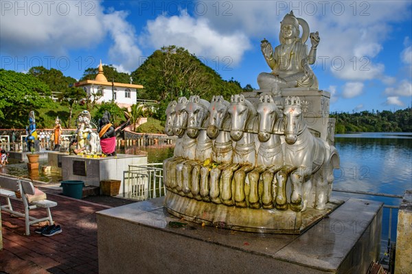 God deity Surya with seven horses personification of sun heat light at religious site largest Hindu sanctuary sanctuary for religion Hinduism outside of India for devout Hindu Hindus in background Sacred lake