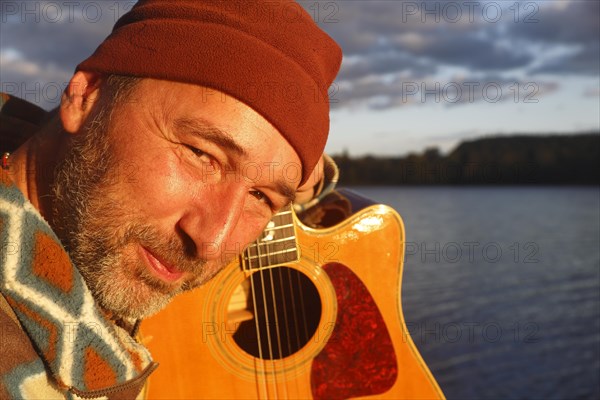 Man playing guitar on a jetty by the lake