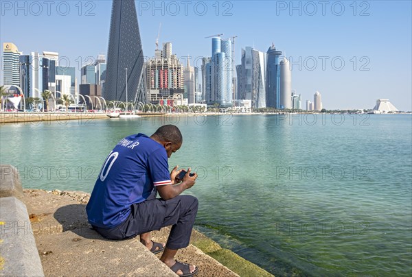 Man sits on steps of Corniche with skyscrapers in background