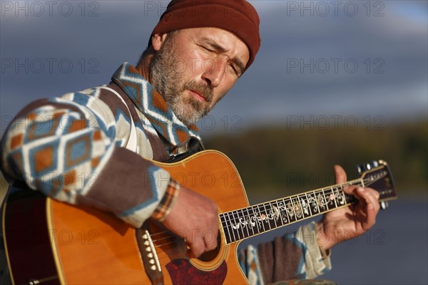 Man playing guitar on a jetty by the lake