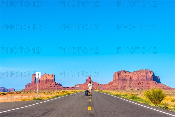 A young Caucasian man with white shirt and green backpack on the road to Monument Valley. Utah