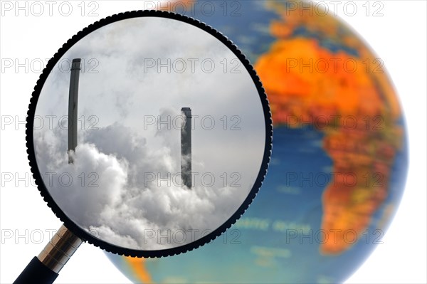 Chimneys covered in smoke seen through magnifying glass held against illuminated terrestrial globe