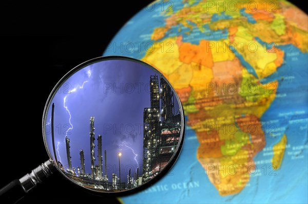 Lightning during thunderstorm above petrochemical industry seen through magnifying glass held against illuminated terrestrial globe