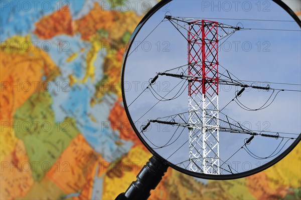 High voltage pylon in red and white through magnifying glass held against illuminated terrestrial globe