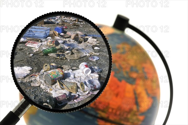Rubbish at refuse dump seen through magnifying glass held against illuminated terrestrial globe