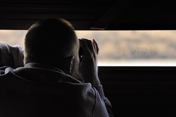 Bird watcher in hide looking through binoculars at waterfowl on lake in the nature reserve Parc du Marquenterre at the Bay of the Somme