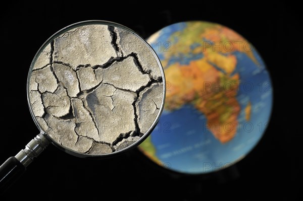 Cracked earth by drought seen through magnifying glass held against illuminated terrestrial globe