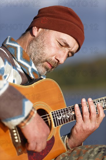 Man playing guitar on a jetty by the lake