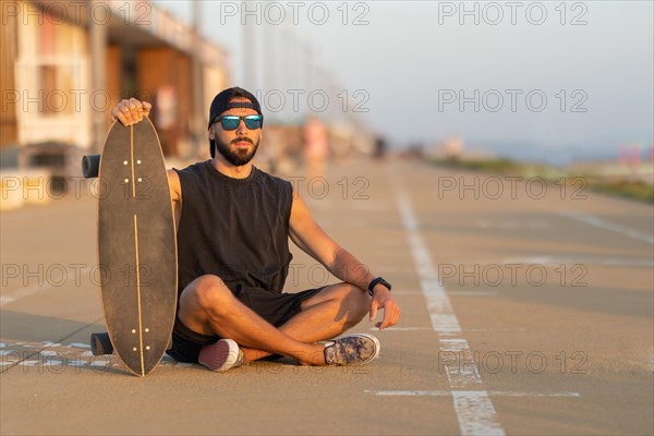 A cool guy sitting on a walking path with his skateboard. Mid shot