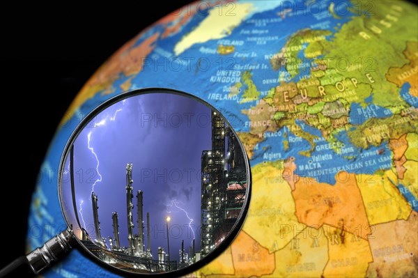 Lightning during thunderstorm above petrochemical industry seen through magnifying glass held against illuminated terrestrial globe