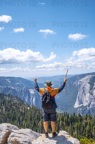 A young man with a walking stick and arms raised at Sentinel Dome in Yosemite National Park. United States