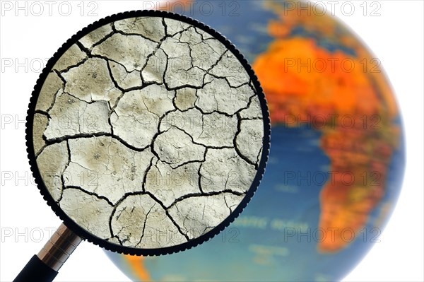 Cracked earth by drought seen through magnifying glass held against illuminated terrestrial globe