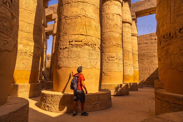 A young tourist walking among the columns with hieroglyphs inside the Karnak Temple
